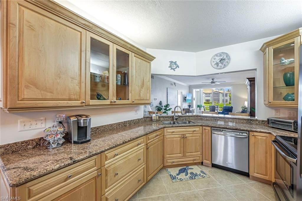 Kitchen featuring appliances with stainless steel finishes, dark stone countertops, light tile patterned floors, ceiling fan, and ornamental molding