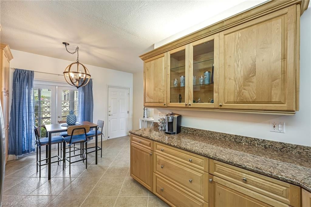 Kitchen with a chandelier, dark stone countertops, glass insert cabinets, hanging light fixtures, and a textured ceiling
