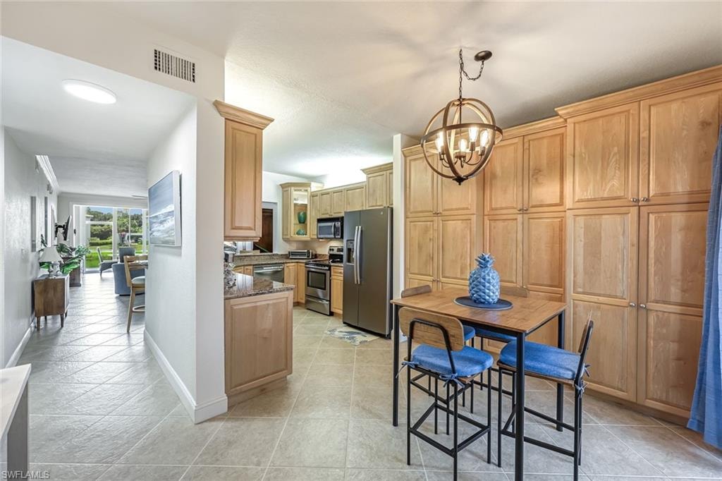 Kitchen with appliances with stainless steel finishes, a chandelier, dark stone countertops, decorative light fixtures, and light tile patterned floors