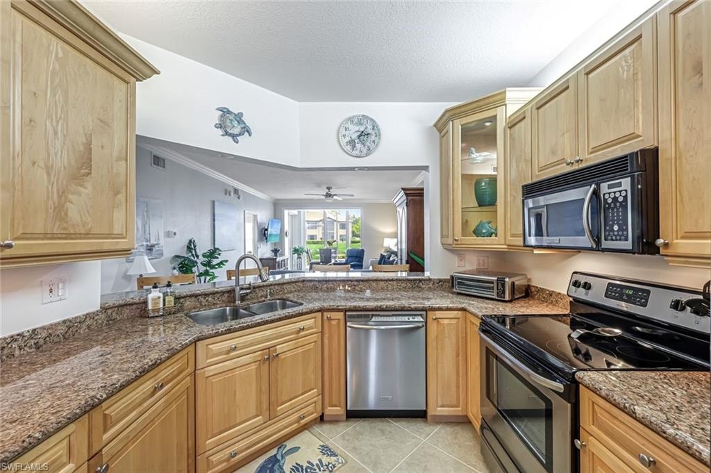 Kitchen featuring appliances with stainless steel finishes, dark stone countertops, a ceiling fan, light tile patterned flooring, and crown molding