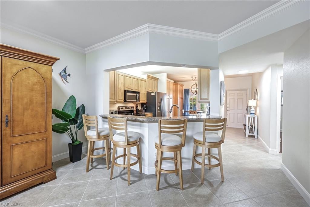 Kitchen with appliances with stainless steel finishes, a kitchen breakfast bar, crown molding, a peninsula, and light tile patterned floors