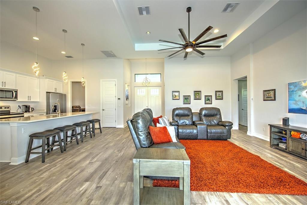 Living room with light hardwood / wood-style flooring, a tray ceiling, a high ceiling, sink, and ceiling fan