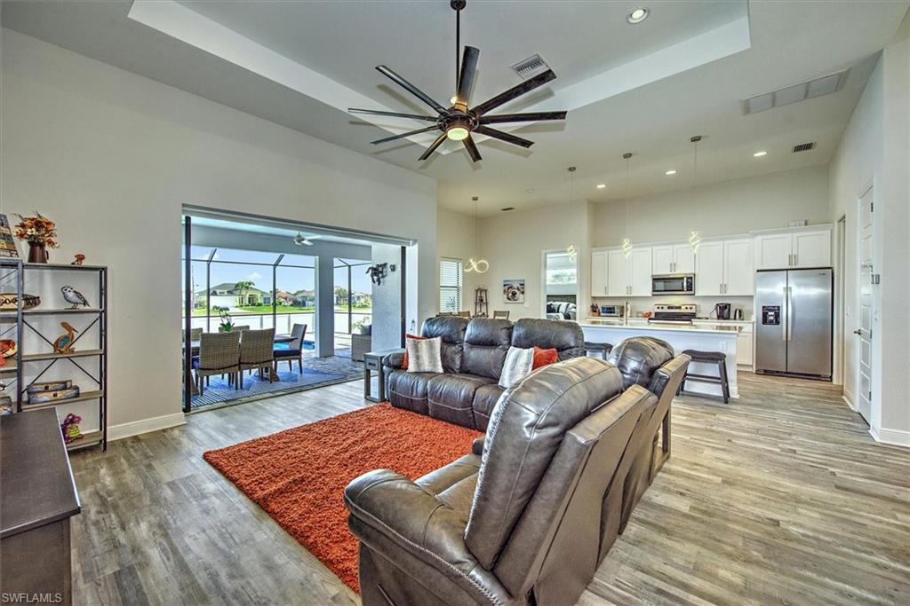 Living room with a raised ceiling, ceiling fan, and light wood-type flooring