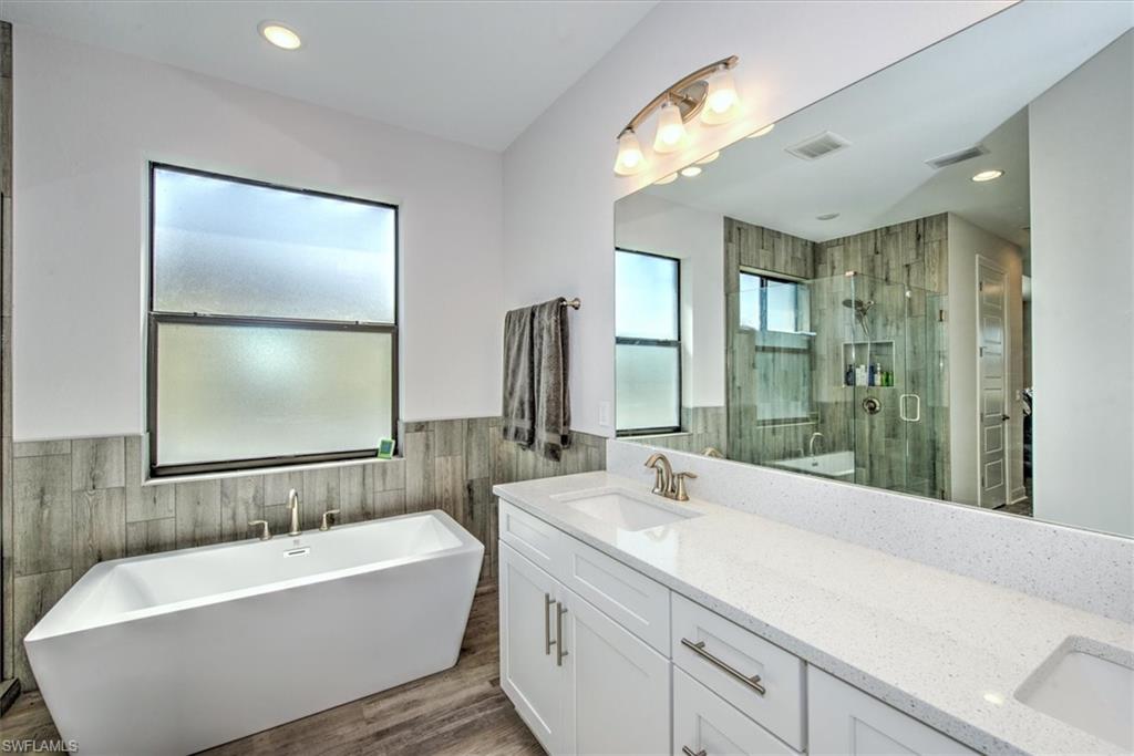 Bathroom with tile walls, hardwood / wood-style flooring, plus walk in shower, and dual bowl vanity