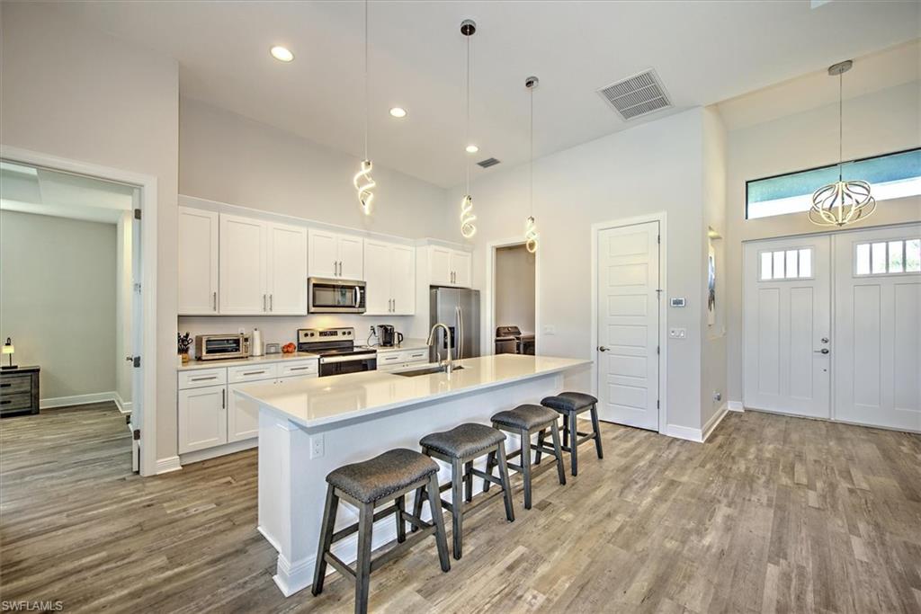 Kitchen with white cabinets, hanging light fixtures, a center island with sink, hardwood / wood-style flooring, and appliances with stainless steel finishes