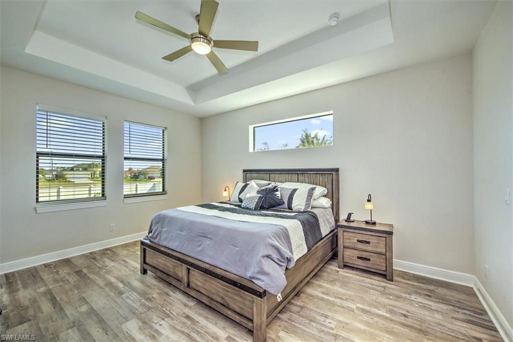 Bedroom with ceiling fan, a raised ceiling, multiple windows, and wood-type flooring
