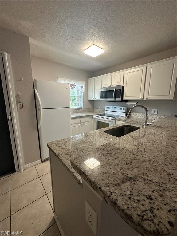 Kitchen featuring granite countertops, white cabinetry, a built-in stainless steel microwave, and tile flooring