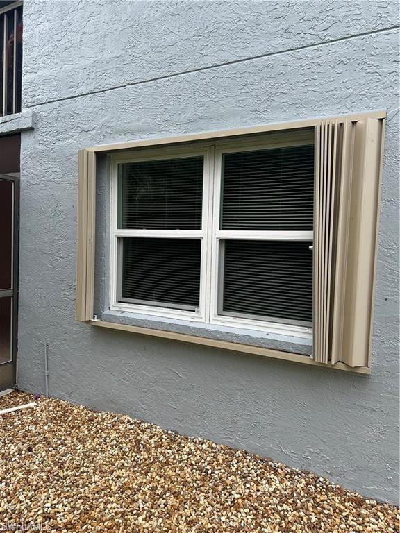 Window with horizontal blinds and tan accordion shutters against a textured stucco exterior