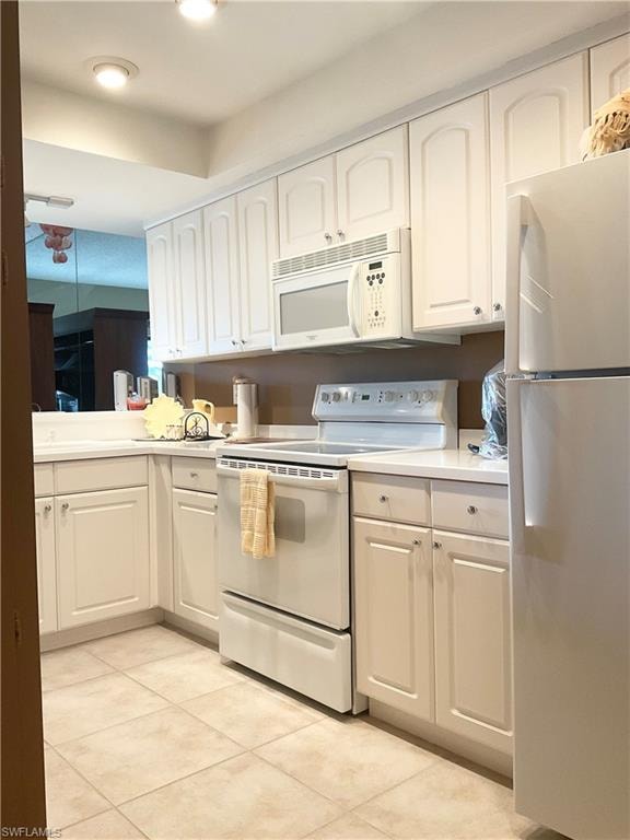 Kitchen featuring light tile floors, white appliances, and white cabinets