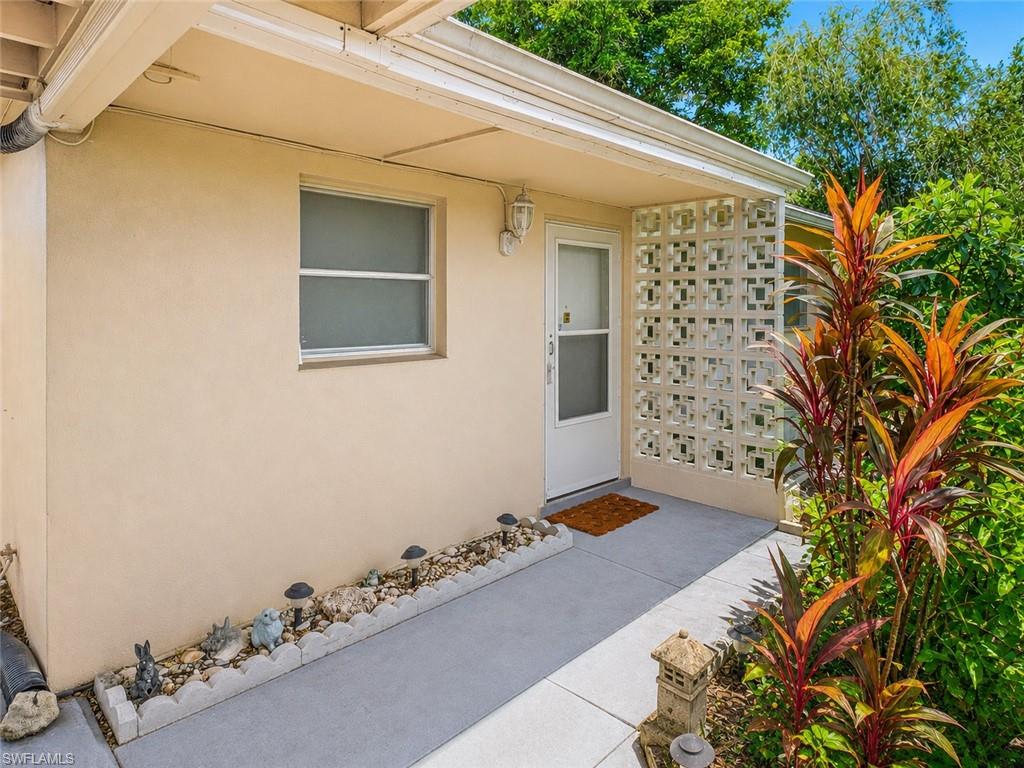 Stucco exterior with a covered entry, concrete walkway, and decorative privacy screen