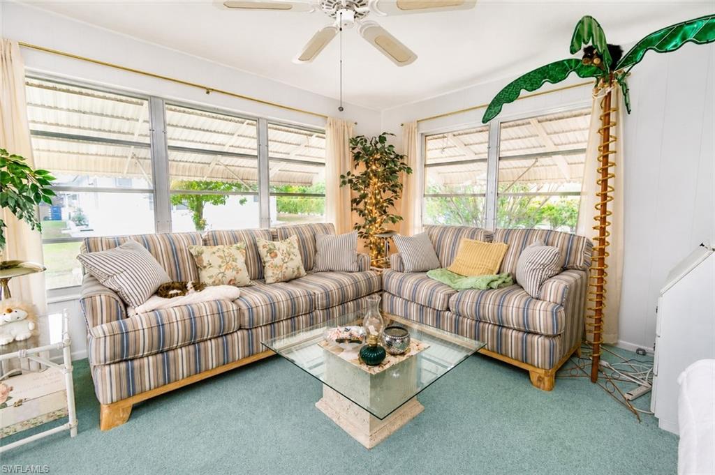 Carpeted living area featuring multiple windows with horizontal blinds, a ceiling fan, and a glass-top coffee table with a stone-finish base