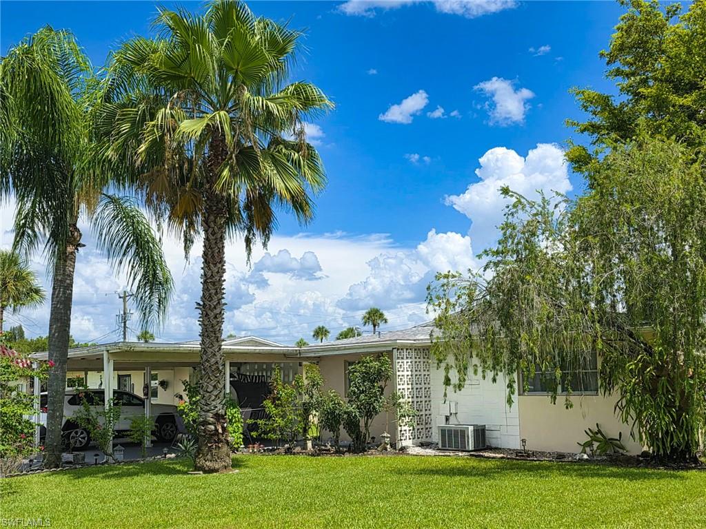Single-story residence featuring a carport, a manicured lawn, and mature palm trees