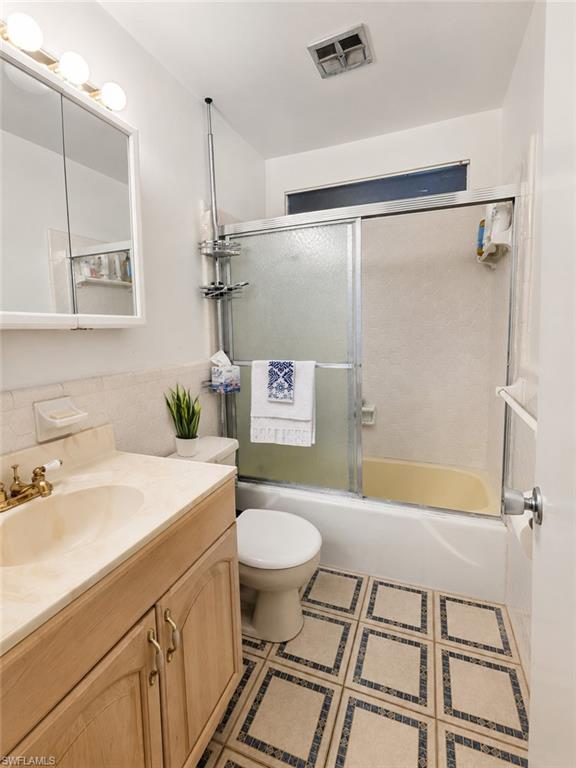 Full bathroom featuring a wood-finish vanity with an integrated sink, patterned floor tiles, a mirrored medicine cabinet, a sliding glass shower door, and an overhead ventilation system