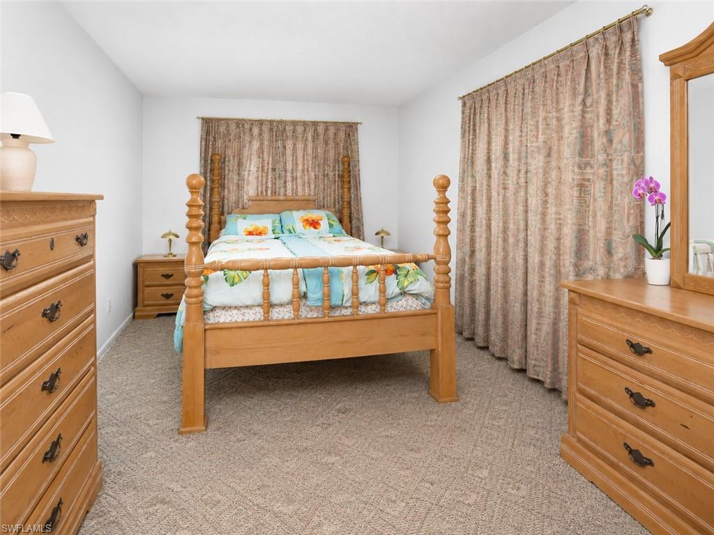 Carpeted room featuring a wooden four-poster bed, window with drapes, and white walls
