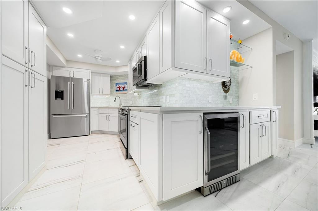 Kitchen featuring tasteful backsplash, light tile patterned flooring, stainless steel appliances, beverage cooler, and white cabinets