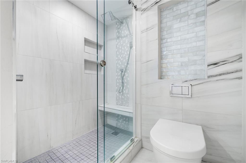 Bathroom featuring tile walls, toilet, and a shower with shower door