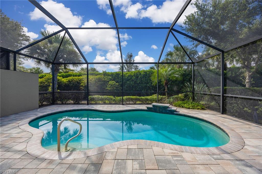 Screened-in pool area featuring a freeform swimming pool , paver decking, and lush perimeter landscaping