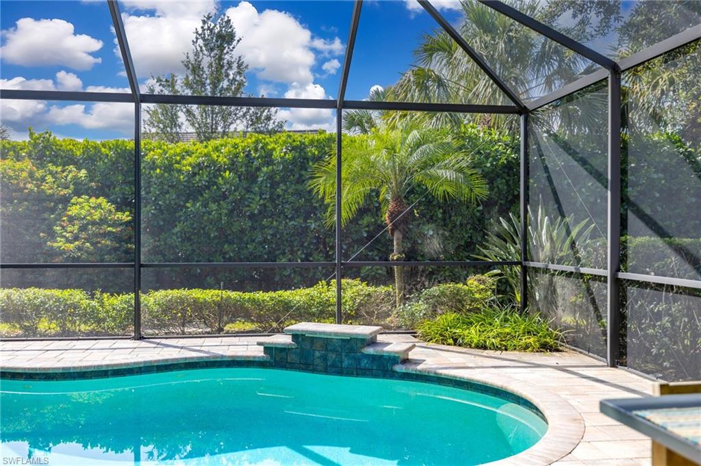 Screened pool area featuring a curved swimming pool with water feature, tile surrounding paver deck, complete private rear yard