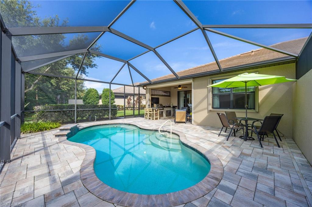 Screened enclosure featuring a freeform pool with waterfall feature and paver decking and electric shutters