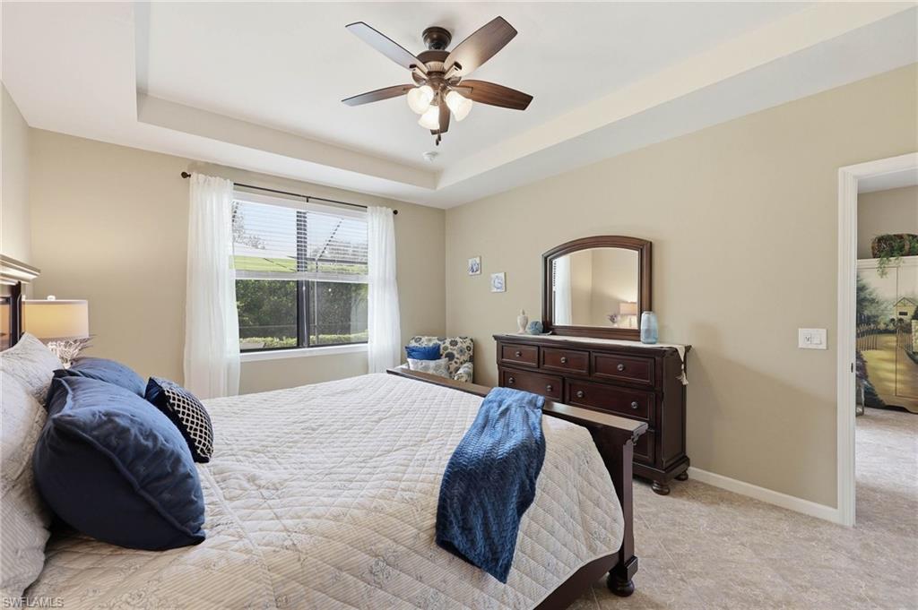 Bedroom featuring a tray ceiling, ceiling fan with integrated lighting, window with blinds, and tile flooring