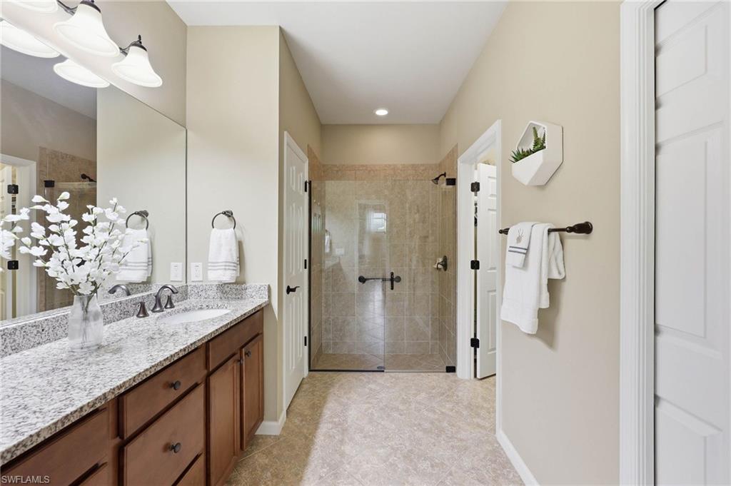 Large primary bathroom with dual-vanity granite countertops, wood cabinetry, walk-in shower, and a separate walk-in closet.