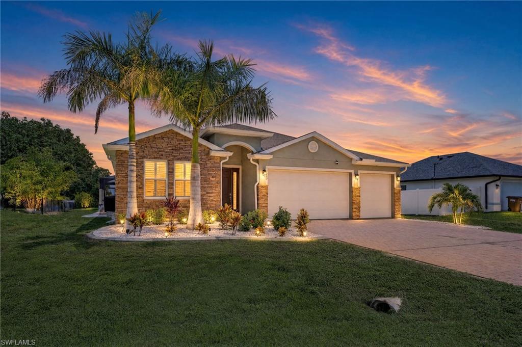 Twilight exterior showcasing exceptional curb appeal in this newer construction Cape Coral home, featuring upgraded exterior lighting, tropical landscaping, and a welcoming front elevation designed to stand out in the Northwest Cape. Ai Dusk Conversion.