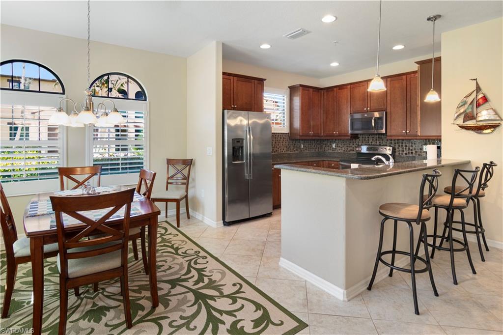Kitchen featuring appliances with stainless steel finishes, backsplash, light tile patterned floors, dark stone counters, and kitchen peninsula