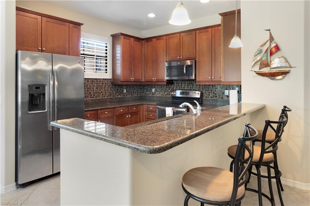 Kitchen with light tile patterned flooring, appliances with stainless steel finishes, hanging light fixtures, and backsplash