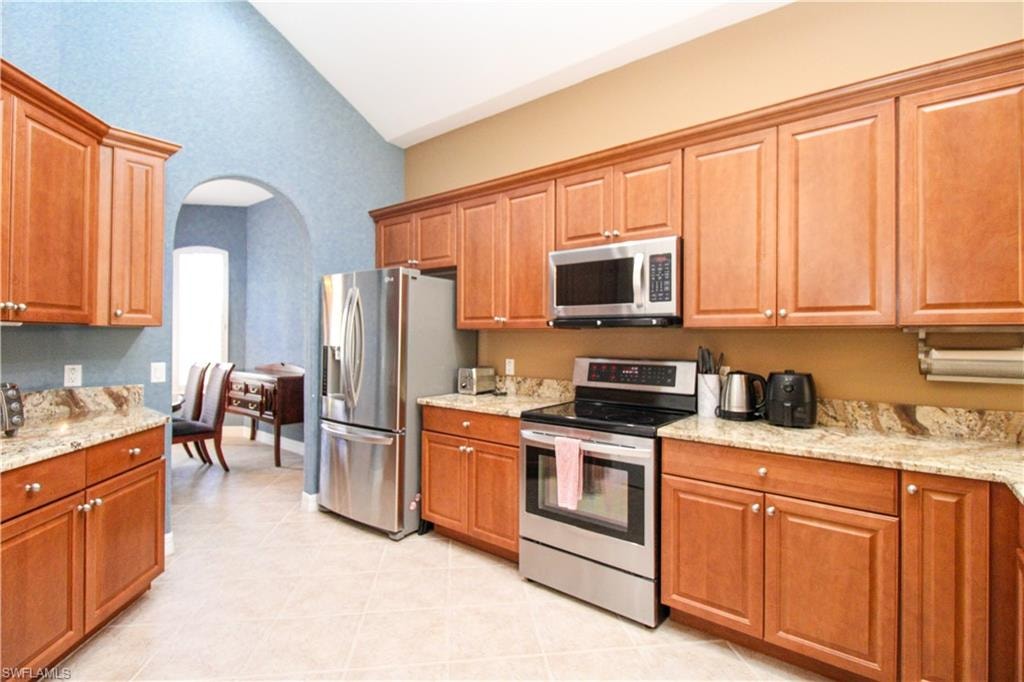 Kitchen featuring light stone counters, appliances with stainless steel finishes, light tile patterned floors, and high vaulted ceiling