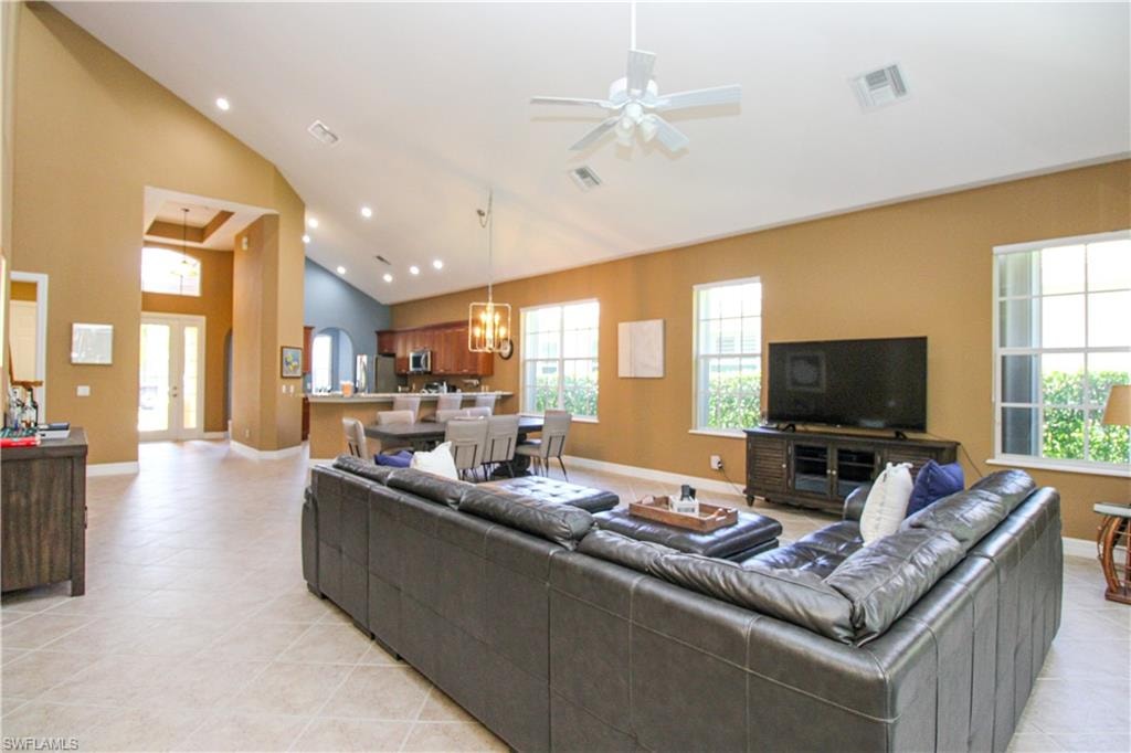 Living room with light tile patterned flooring, high vaulted ceiling, and ceiling fan with notable chandelier