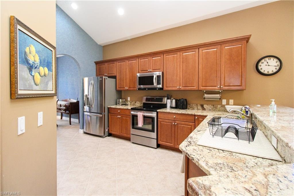 Kitchen featuring sink, light stone countertops, appliances with stainless steel finishes, lofted ceiling, and light tile patterned floors