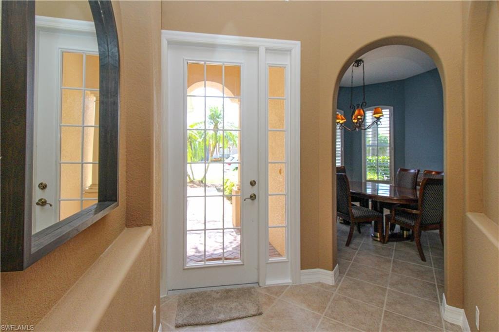 Tiled foyer entrance with a notable chandelier, french doors, and plenty of natural light