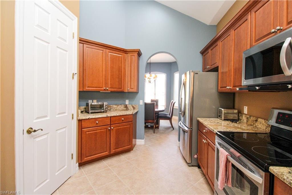 Kitchen with light tile patterned flooring, a chandelier, light stone counters, stainless steel appliances, and a towering ceiling