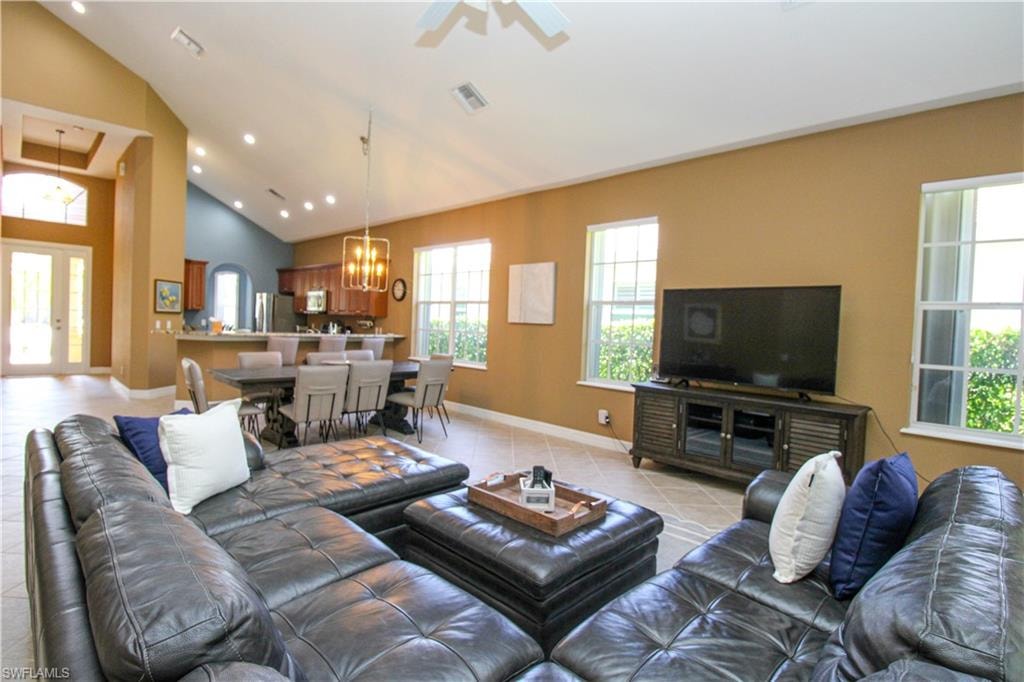 Living room featuring ceiling fan with notable chandelier, light tile patterned floors, and high vaulted ceiling