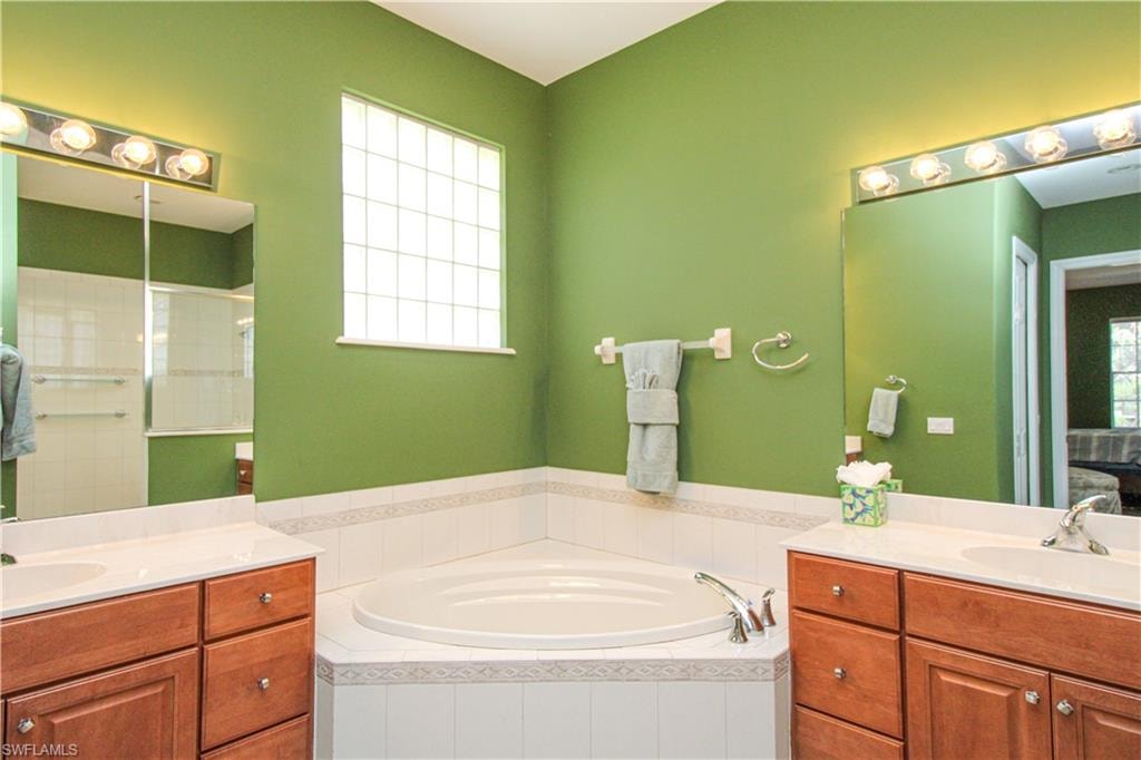 Bathroom featuring double vanity, tiled bath, and a wealth of natural light
