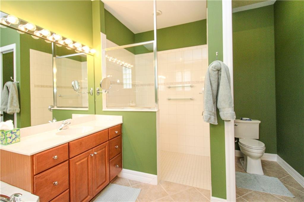 Bathroom featuring tile patterned floors, vanity, a tile shower, and toilet