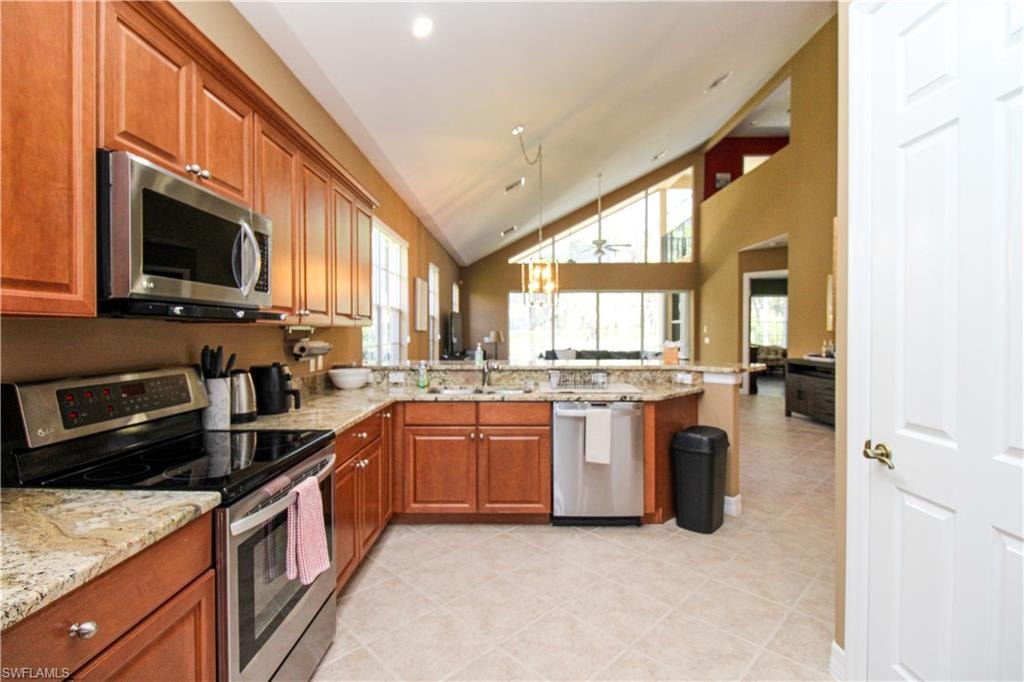 Kitchen featuring kitchen peninsula, appliances with stainless steel finishes, light tile patterned floors, and light stone counters