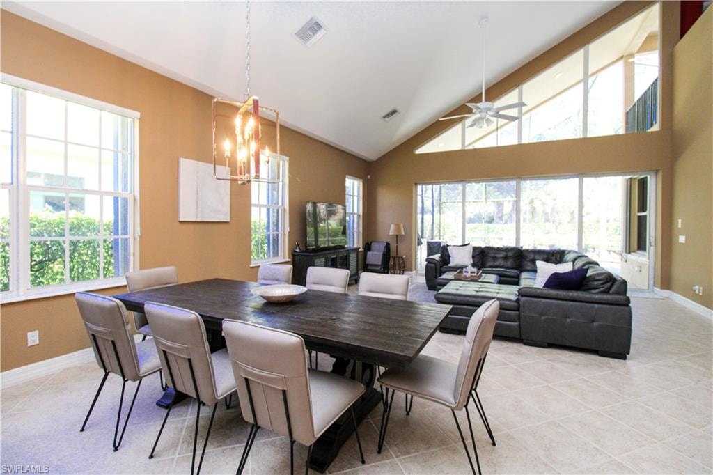Tiled dining area with ceiling fan with notable chandelier, a healthy amount of sunlight, and high vaulted ceiling