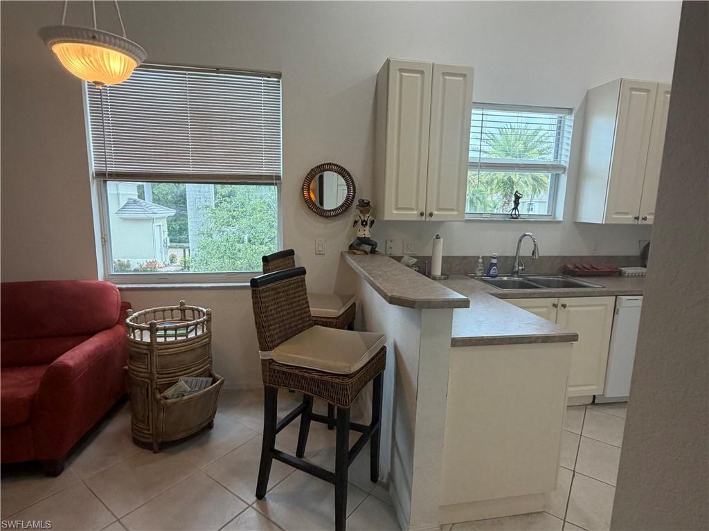 Kitchen space featuring a double basin stainless steel sink with a gooseneck faucet, light-toned countertops, white cabinetry with silver-toned hardware, and a breakfast bar