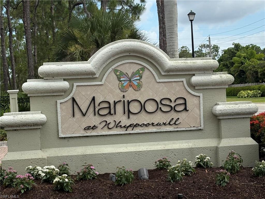 Community entrance monument featuring textured stucco finish, decorative tile inlay with butterfly motif, dimensional lettering, and integrated landscaping with flowering shrubs