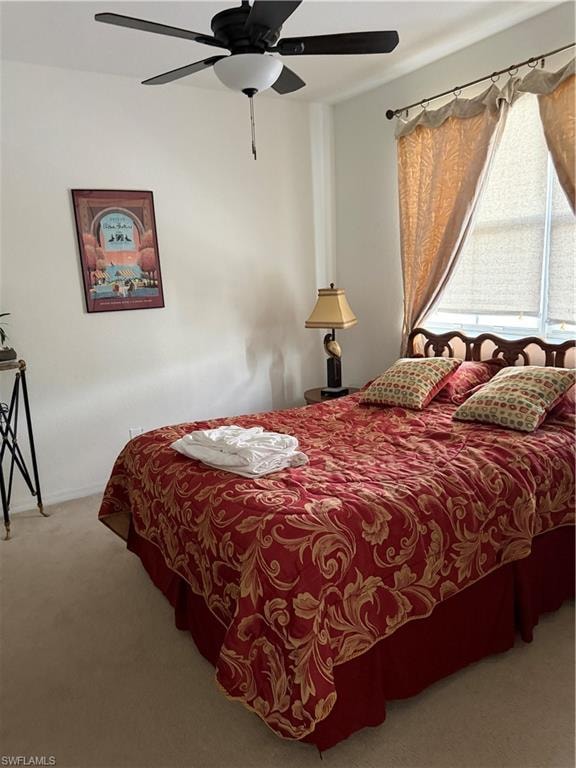 Bedroom featuring light neutral wall paint, a ceiling fan with integrated lighting, a window with roller shades and decorative drapes, and light-toned carpet flooring