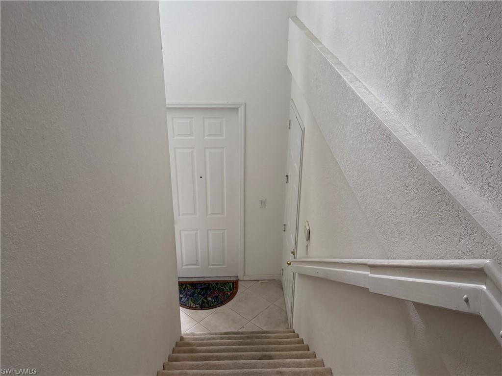 Entryway featuring a paneled door with a peephole, light-toned walls, and a staircase with a carpeted runner and a white handrail