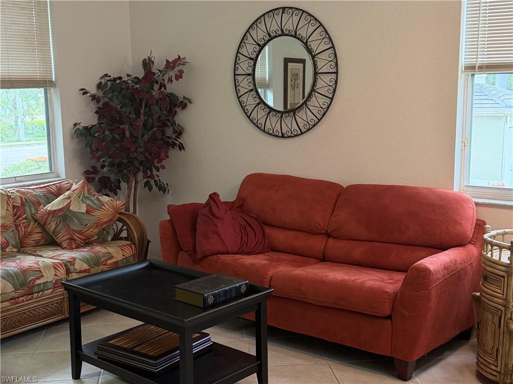 Living area featuring light-toned walls, tile flooring, and multiple windows with horizontal blinds