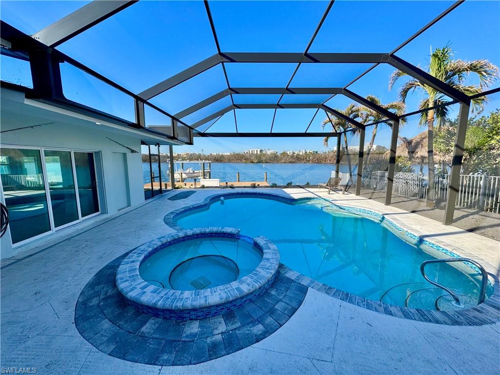 View of swimming pool featuring an in ground hot tub, a patio, a water view, and glass enclosure