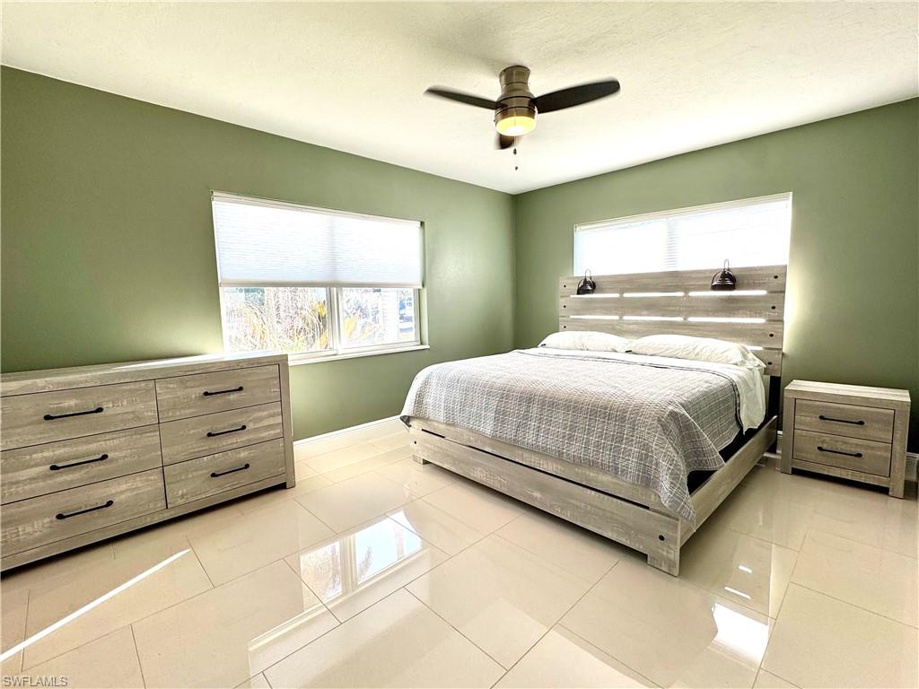 Tiled bedroom featuring multiple windows and ceiling fan