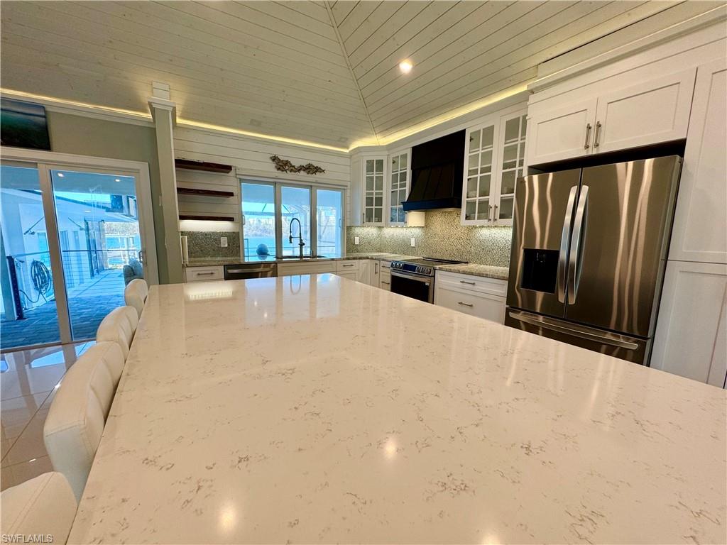 Kitchen featuring white cabinetry, light stone countertops, premium range hood, lofted ceiling, and appliances with stainless steel finishes