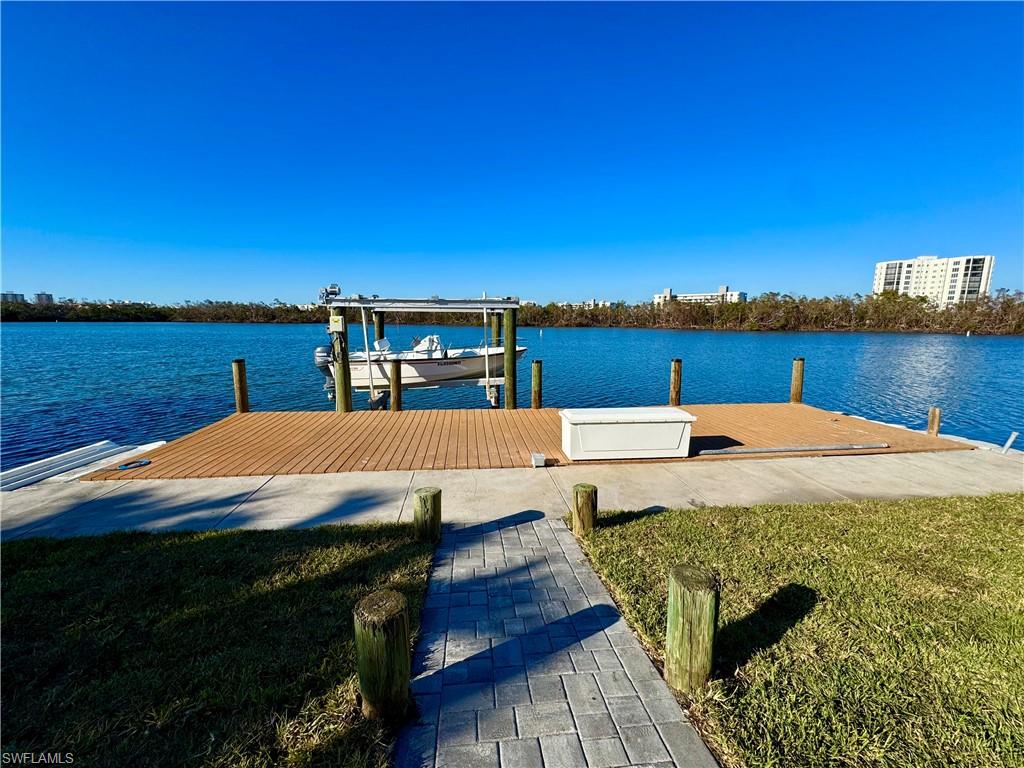 View of dock with a lawn and a water view