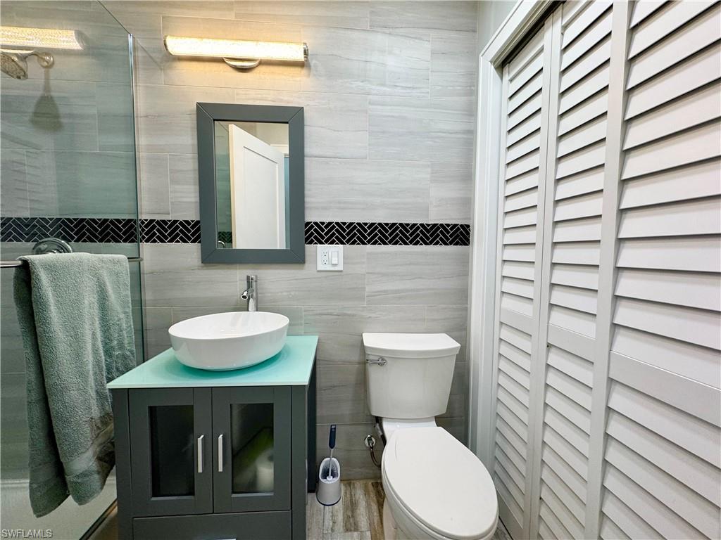 Bathroom featuring vanity, toilet, tile walls, and a shower with shower door