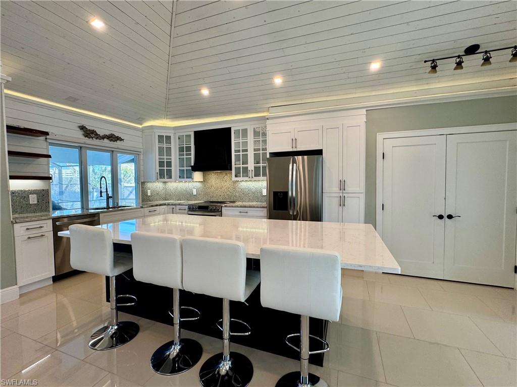 Kitchen with appliances with stainless steel finishes, white cabinetry, a kitchen island, and custom range hood