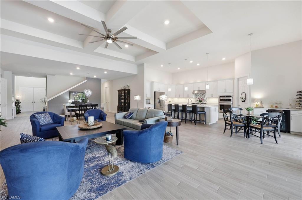 Open-concept living space featuring high tray ceilings, wood tile flooring, a contemporary ceiling fan, recessed lighting, and a kitchen with white cabinetry and upgraded  stainless steel appliances